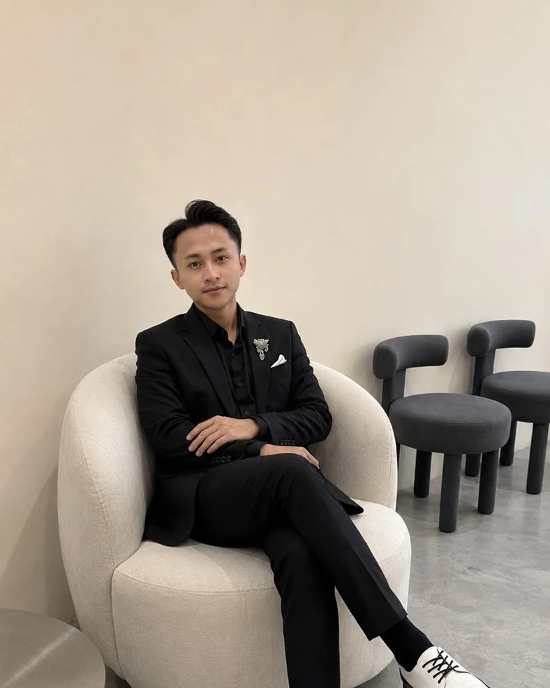 Potret hitam-putih Rihul CZ duduk mengenakan setelan hitam